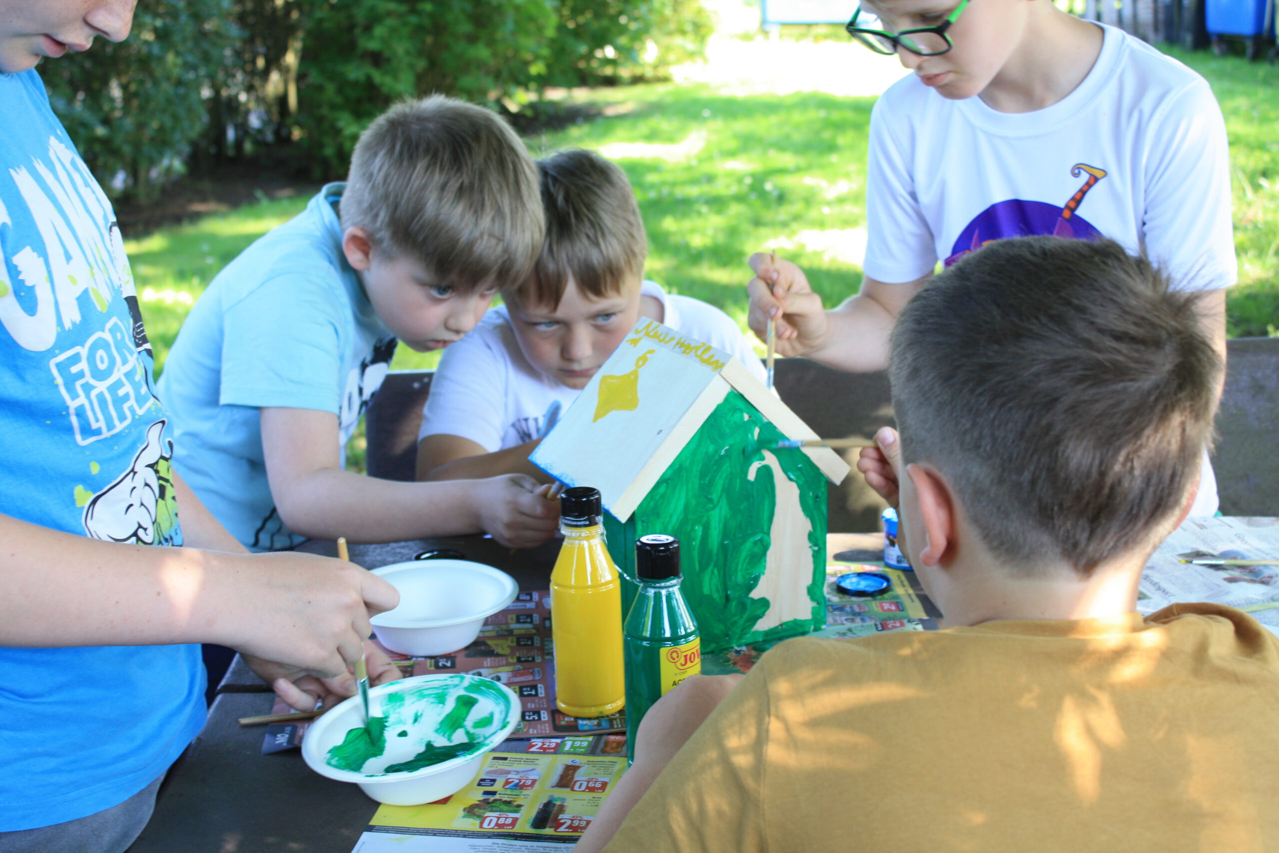 Kinder bemalen ein Vogelhaus mit bunten Farben